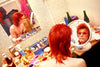 david bowie as ziggy stardust sits with a red mullet hairstyle and face makeup is seated at a cluttered vanity with circle mirror, looking into a mirror. Various cosmetics and bottles are visible on the table. Another mirror shows their reflection. Hand signed print by photographer Mick Rock.
