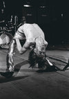 A black and white photo of Iggy Pop bent backwards while performing. Shot by Mick Rock. 
