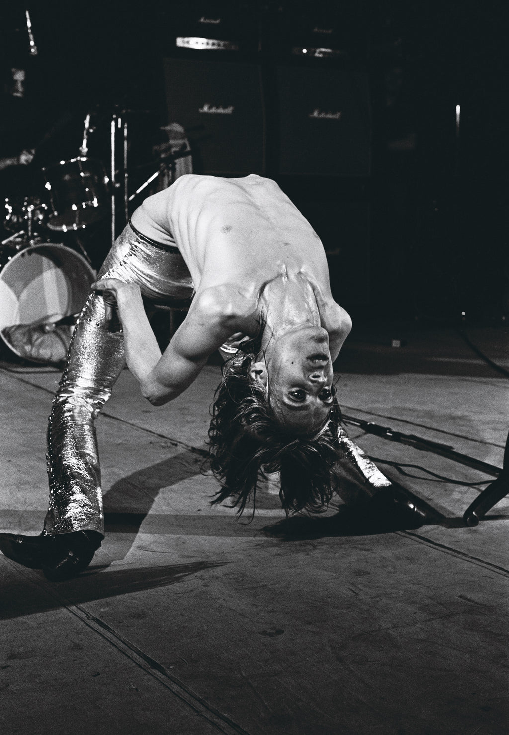 A black and white photo of Iggy Pop bent backwards while performing. Shot by Mick Rock. 