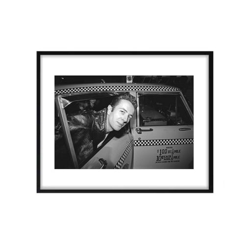 A photo of Joe Strummer of The Clash sitting in a nyc taxi with his head out the window. 
