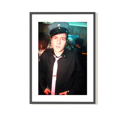 Framed photo of Joe Strummer of The Clash standing wearing a military hat and tie. 