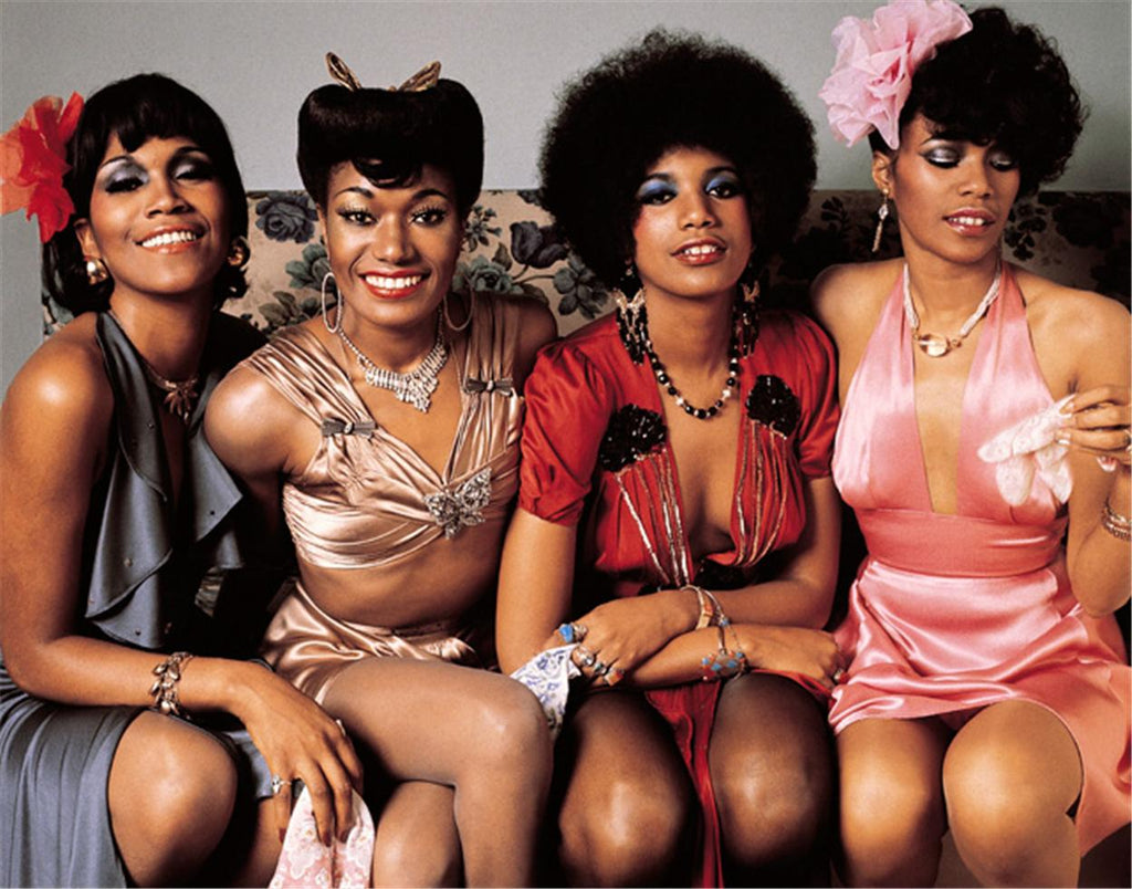 A photograph of the Pointer Sisters, featuring three smiling women dressed in vintage fashion, with a focus on their hairstyles and the textured background.