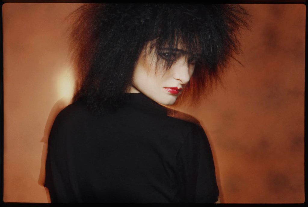 Siouxsie Sioux photographed with big black hair and gold background at Bow Street Studio. 
