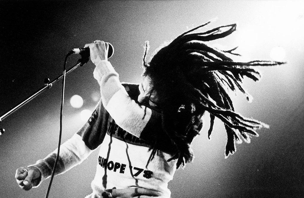 Black and white photograph of Bob Marley performing in England, dancing with microphone in view.