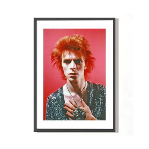 A fine art limited edition print of David Bowie with red hair, wearing a glittery shirt on a pink background, posed with a serious expression.