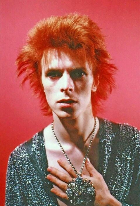 A fine art limited edition print of David Bowie with red hair, wearing a glittery shirt on a pink background, posed with a serious expression.