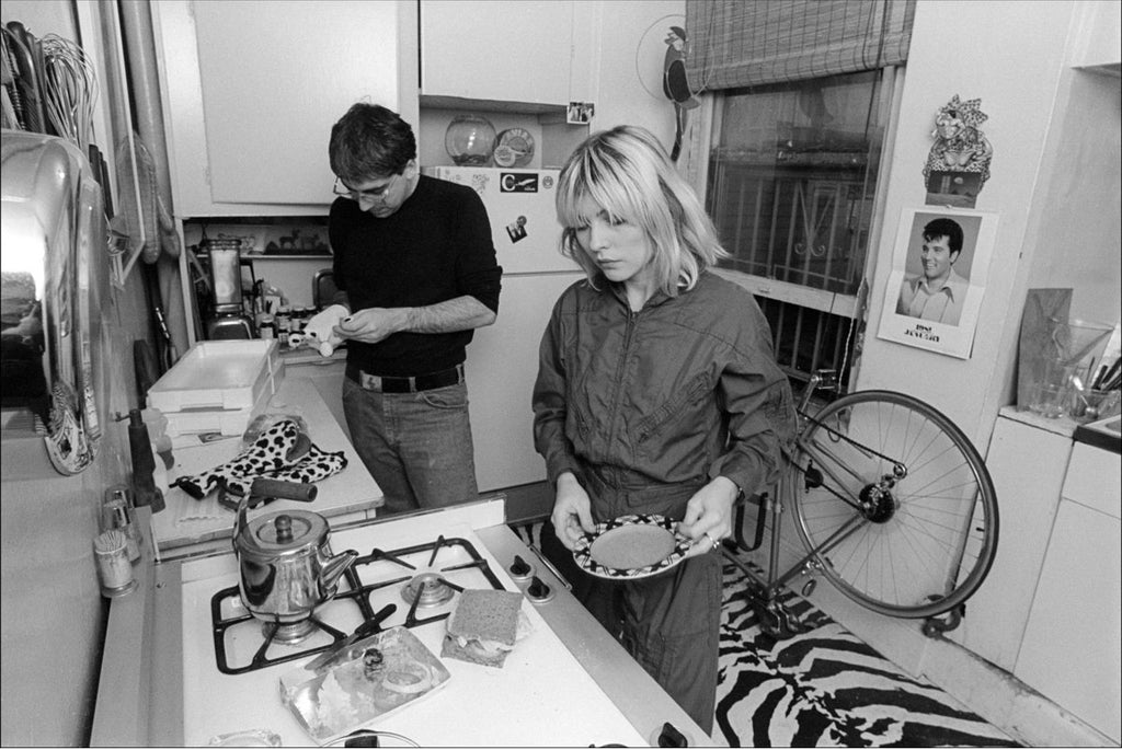 A black and white photograph of Debbie Harry and Chris Stein of Blondie in a kitchen setting, taken by Allan Tannenbaum in 1980.