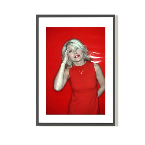 A photograph of Debbie Harry in a red dress, with a red salute, against a red background. The image is a vintage Allan Tannenbaum photograph.