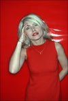A photograph of Debbie Harry in a red dress, with a red salute, against a red background. The image is a vintage Allan Tannenbaum photograph.