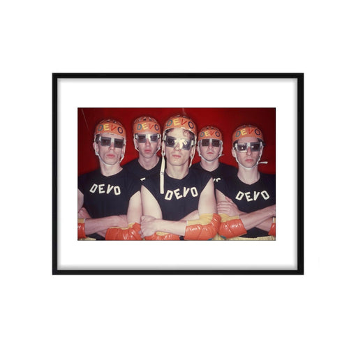 A group photograph of the Devo band members wearing similar black and orange outfits, posing with their iconic orange helmets.