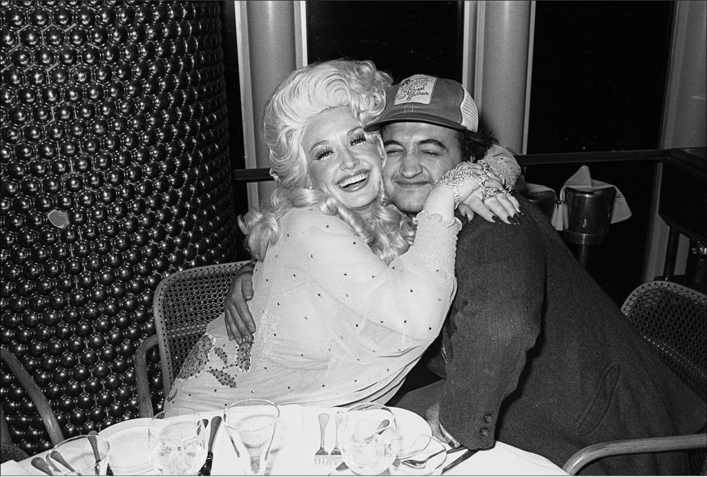 Black and white photo of Dolly Parton and John Belushi hugging. Photo taken at Windows on the World for her Bottom Line concert after-party, May 1977.