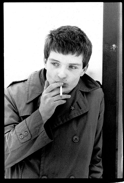 Ian Curtis of Joy Division smoking a cigarette outside in 1979, photo captured by Kevin Cummins. 