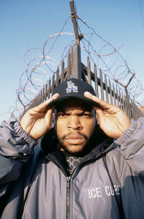 Rapper and actor Ice Cube photographed in front of wire fence with LA hat. Photo shot by Kevin Cummins. 