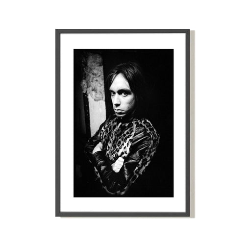 black and white portrait of Iggy Pop wearing a leopard print jacket with his arms crossed. Shot by photographer Mick Rock. 