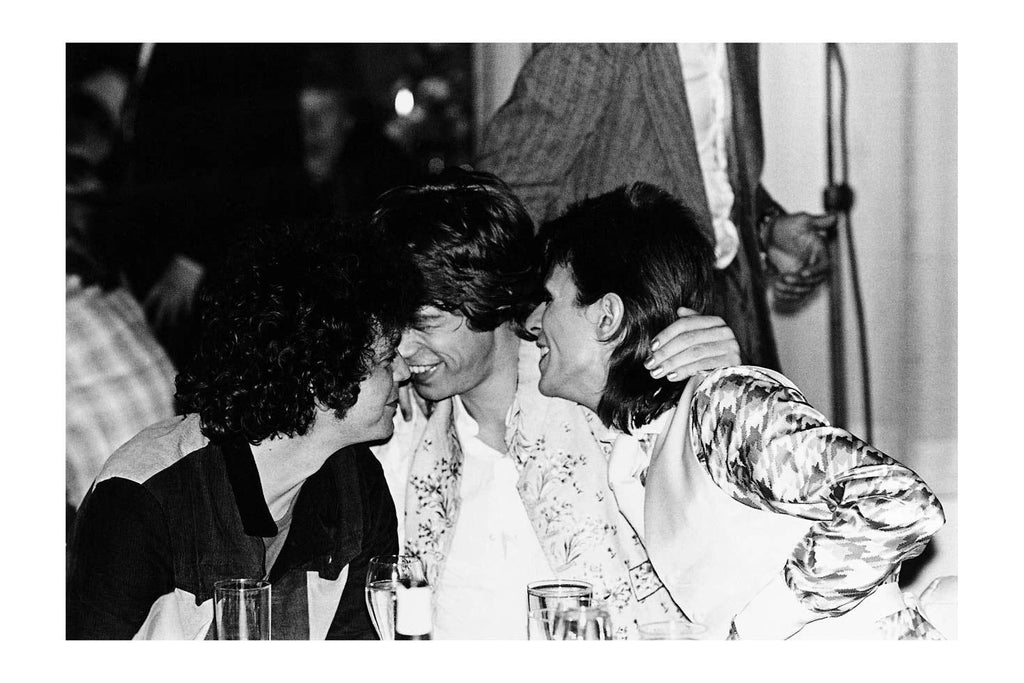 a fine art print of david bowie, mick jagger and lou reed hugging at a table in nyc. shot by Mick Rock. 