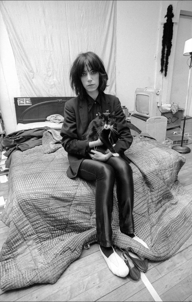 A black and white photo of singer and poet Patti Smith in her apartment in NYC with her cat. 