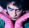 A close up shot of Tim Curry from The Rocky Horror Picture Show wearing pink gloves and dark eye makeup, taken by Mick Rock. 