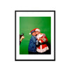 A photograph of Truman Capote and Andy Warhol wearing a Santa Claus hat hugging against a green background. 