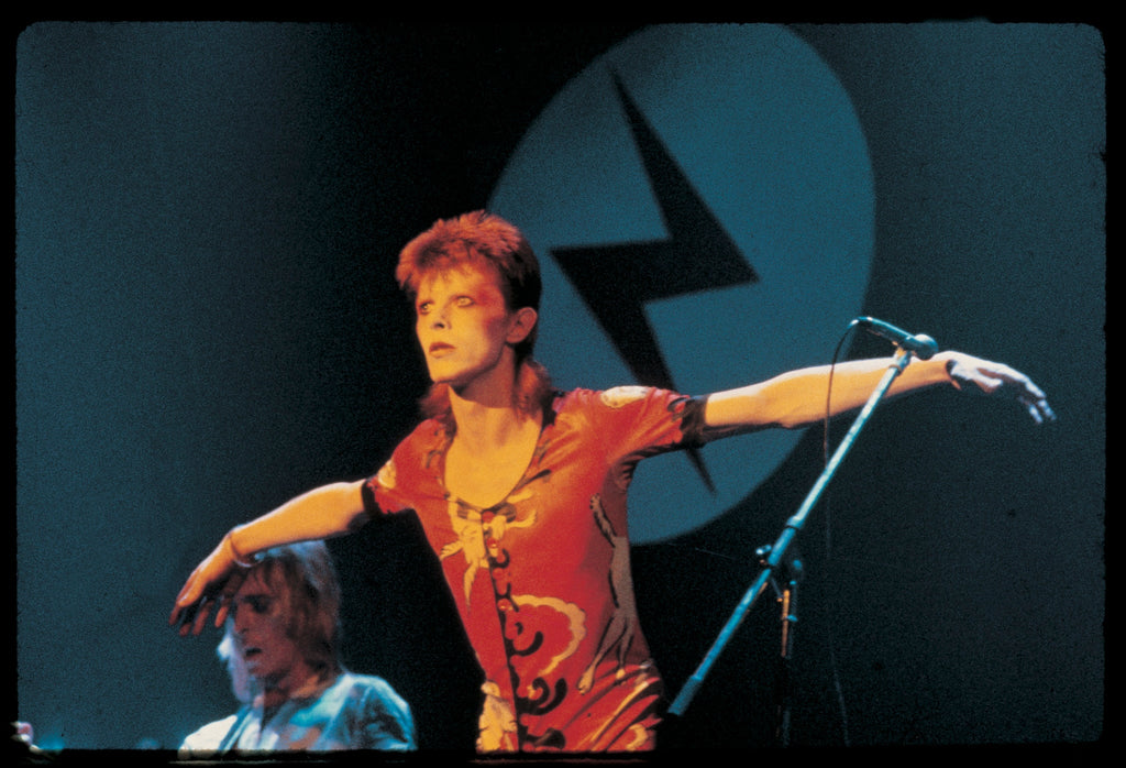 A photograph of David Bowie performing, capturing his form and facial expression. The image is embossed with a signature stamp and is part of a limited edition collection.