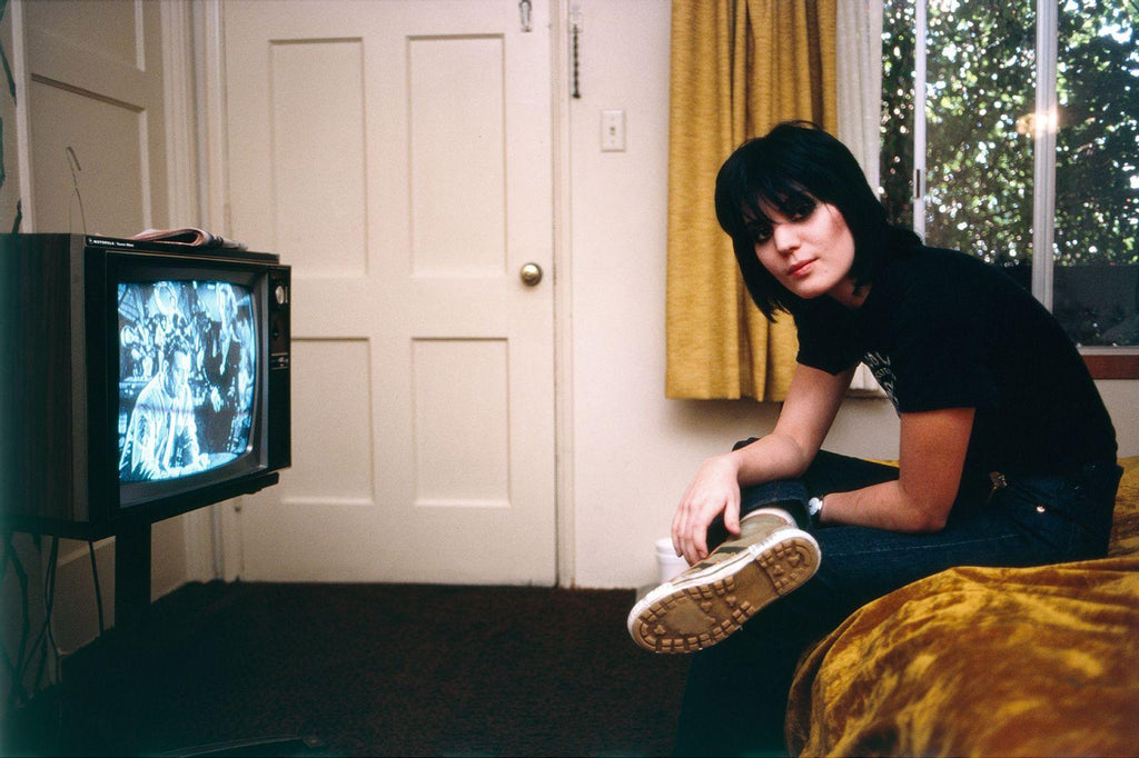 Joan Jett sitting in a hotel room with the TV on, captured by photographer Brad Elterman. 